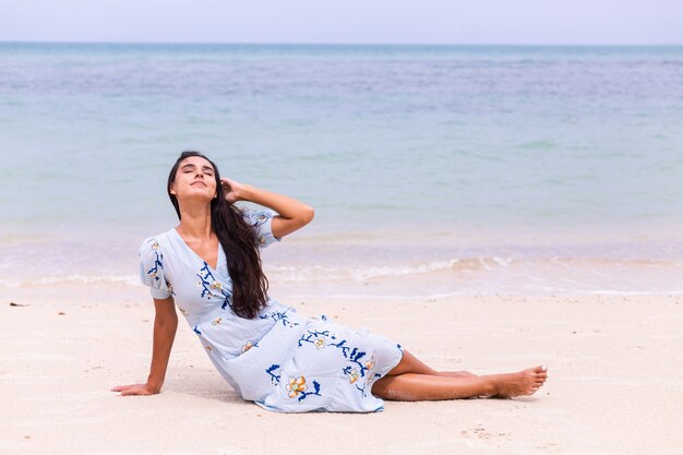 Retrato romântico de mulher com vestido longo azul na praia à beira-mar em dia de vento