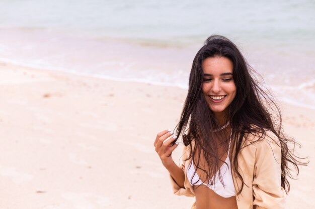 Retrato romântico de mulher na praia em dia de vento, luz quente do sol.