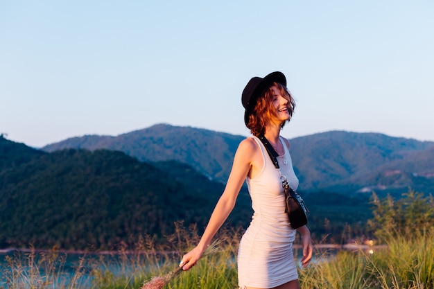 Retrato romântico de uma jovem mulher caucasiana com vestido de verão relaxando no parque na montanha com vista para o mar tropical. Mulher em viagens de férias pela Tailândia Mulher feliz ao pôr do sol