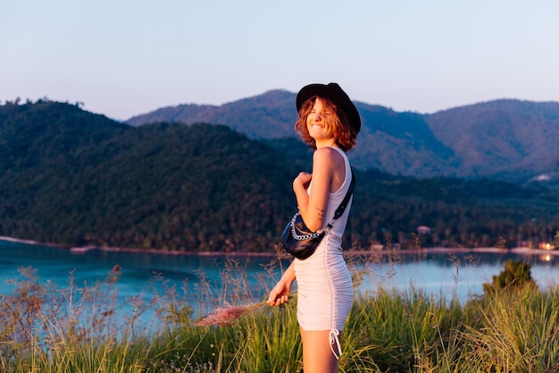 Retrato romântico de uma jovem mulher caucasiana com vestido de verão relaxando no parque na montanha com vista para o mar tropical. mulher em viagens de férias pela tailândia mulher feliz ao pôr do sol