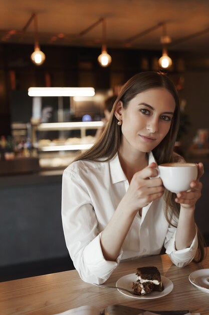 Retrato vertical de romântico feminino jovem bebendo café sozinho em um café aconchegante.