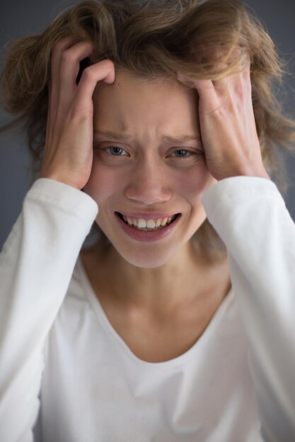 Retrato vertical de uma jovem chorando frustrada olhando para a câmera enquanto segura as mãos na cabeça