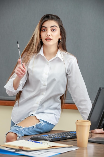 Retrato vertical de uma jovem levantou a caneta e sentado na mesa