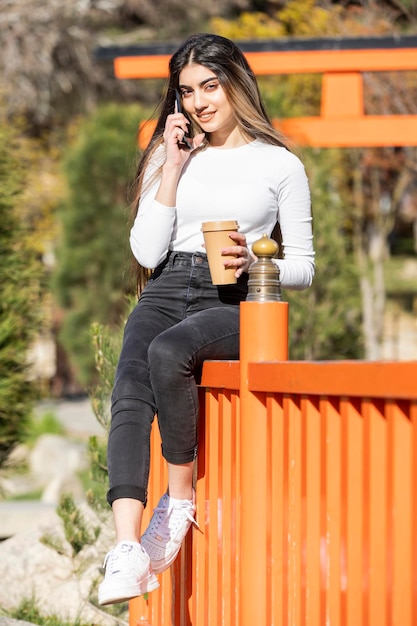 Foto grátis retrato vertical de uma jovem linda falando ao telefone e olhando para a câmera foto de alta qualidade