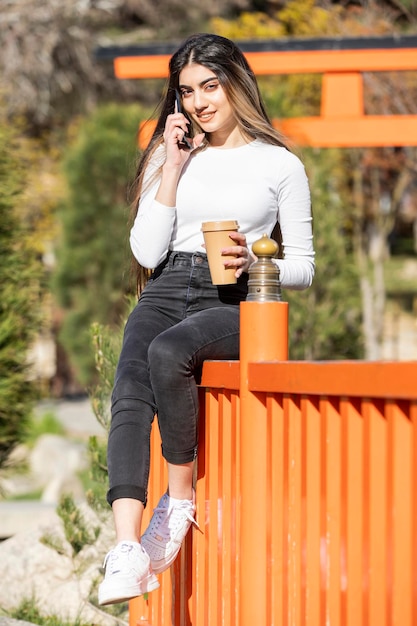 Retrato vertical de uma jovem linda falando ao telefone e olhando para a câmera Foto de alta qualidade