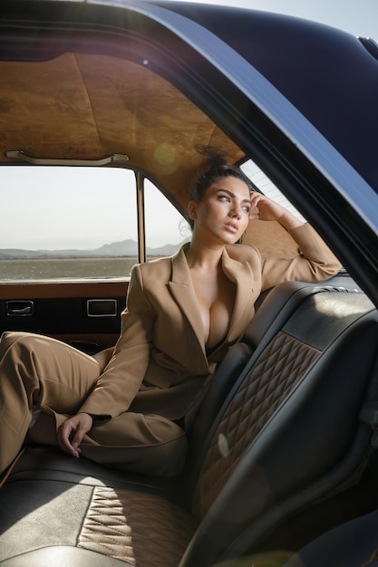 Retrato vertical do jovem modelo sentado no banco traseiro do carro 39 e olhando de lado Foto de alta qualidade