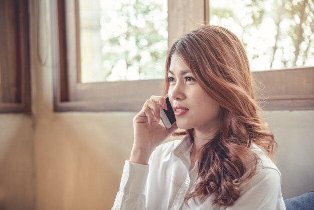 Retratos da bela mulher asiática, a confiança é de pé e segurando o celular