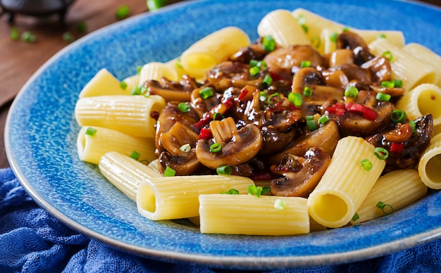 Rigatoni de massa vegetariana com cogumelos e malagueta na tigela azul na mesa de madeira. comida vegana.