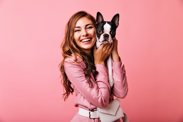 Rindo linda mulher segurando seu cachorro. retrato de gengibre linda garota posando em rosa com buldogue francês.