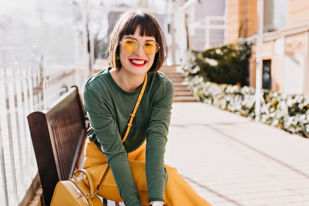 Rindo mulher elegante relaxando após o passeio de primavera. Foto ao ar livre de uma linda senhora morena sentada no banco.