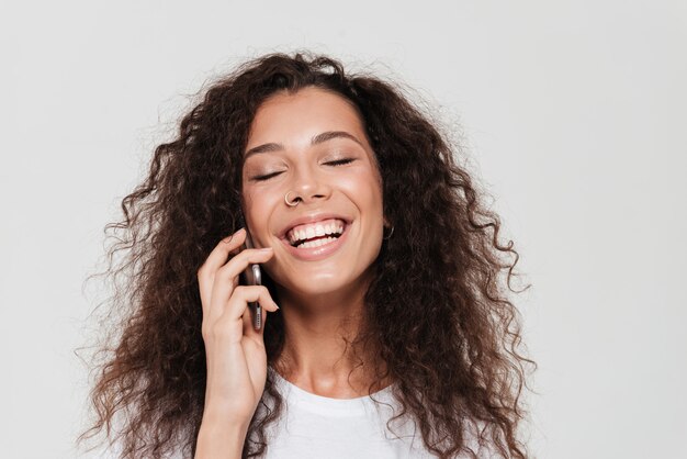 Rindo mulher encaracolada que falando pelo smartphone