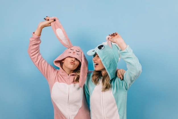 Rindo senhoras atraentes posando em kigurumi garota despreocupada em traje de coelho em pé sobre fundo azul