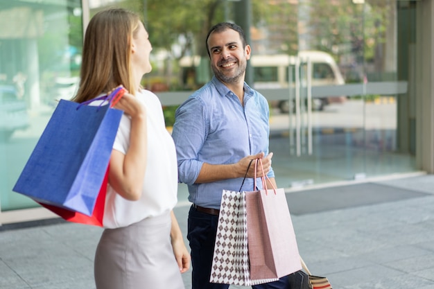 Rir, par, shopping, segurando, sacolas papel, andar, e, olhando um ao outro