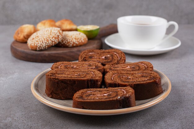 Rolinho de bolo de chocolate no prato de cerâmica com chá preto