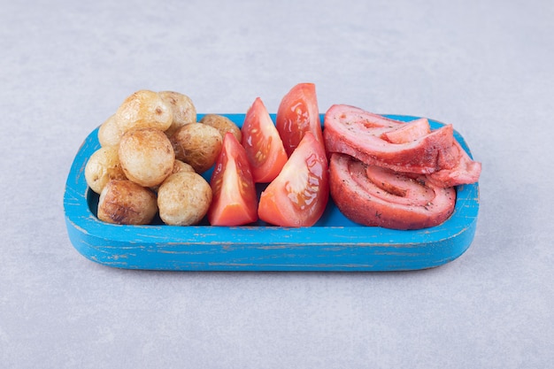 Rolinhos de presunto, tomate e batatas fritas na placa azul.