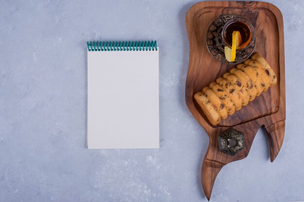 Rollcake servido com chá Earl Grey em uma travessa de madeira com um caderno de lado