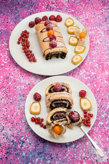 Rolo de fatias de bolo com frutas diferentes dentro de um prato branco no fundo colorido bolo de biscoito doce