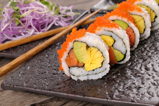 rolo de sushi com pauzinhos em uma placa preta