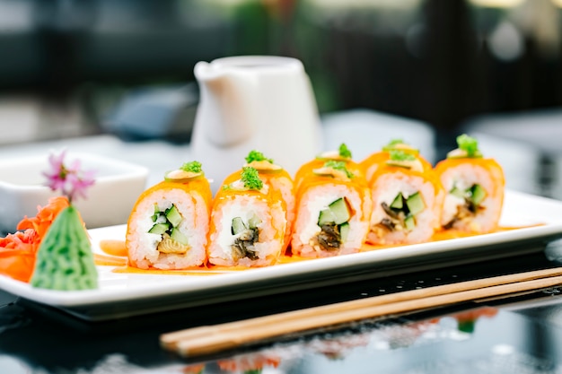 Rolo de sushi laranja com pepino e peixe, guarnecido com tobiko verde