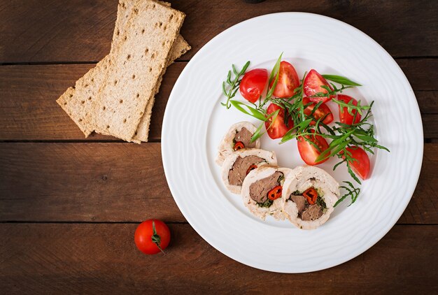 Rolos de frango assado dieta fígado recheado, pimentão e ervas com uma salada de tomate e rúcula. Menu dietético. Nutrição apropriada. Vista do topo