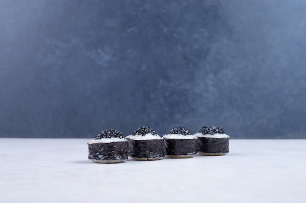 Rolos de Maki decorados com caviar preto na mesa branca.