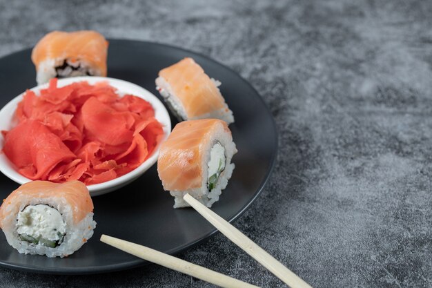 Rolos de salmão em uma travessa preta com gengibre vermelho marinado.