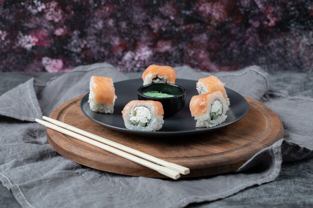 Rolos de salmão em uma travessa preta com molho de wasabi.