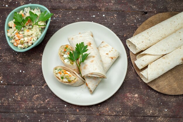 Rolos de sanduíche lavash com vista de cima fatiados com salada e carne dentro junto com salada em uma mesa de madeira.