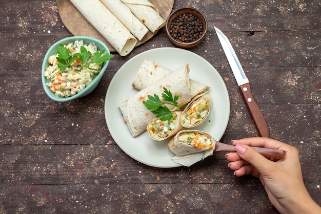 Rolos de sanduíche lavash com vista de cima fatiados com salada e carne dentro junto com salada em uma mesa de madeira.