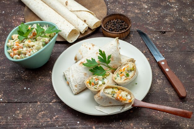 Rolos de sanduíche lavash com vista de cima fatiados com salada e carne dentro junto com salada na mesa de madeira.