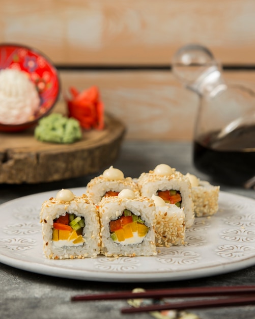 Rolos de sushi com pimentão vermelho e amarelo, pepino coberto com gergelim