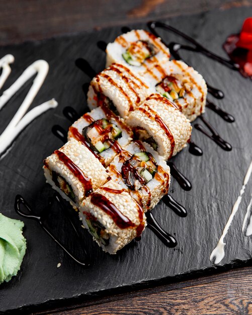 Rolos de sushi com sementes de gergelim, servidos com molho e wasabi