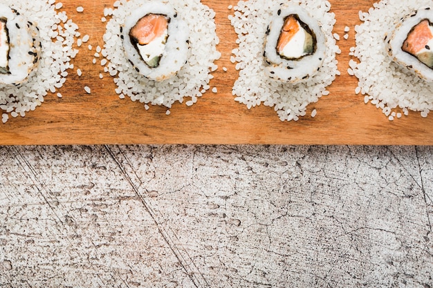 Foto grátis rolos de sushi dispostos em arroz cru sobre a bandeja de madeira