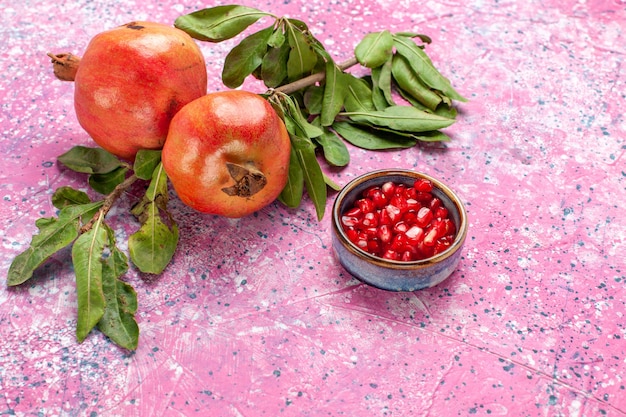 Romã fresca com folhas verdes na superfície rosa