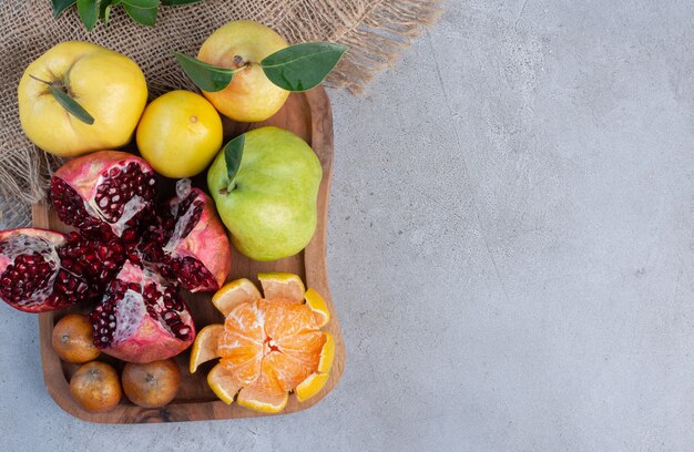 Romã quebrada, tangerina descascada e marmelos inteiros e peras em um pedaço de pano com fundo de mármore.