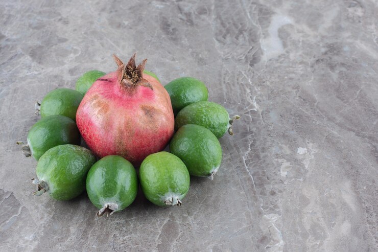 Foto grátis romã rodeada de feijoas em superfície de mármore