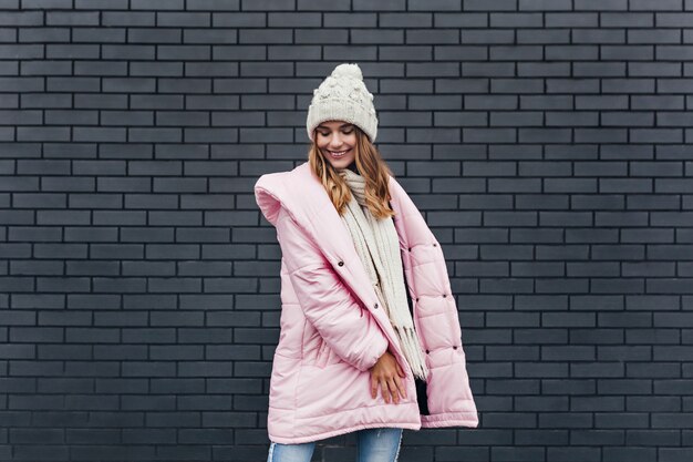 Foto grátis romântica garota europeia com casaco rosa, sorrindo em dia frio. mulher de cabelos louros alegre se divertindo durante a sessão de fotos de inverno.