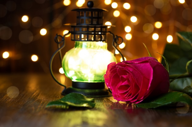 Rosa vermelha e lanterna com luzes sobre uma mesa de madeira.