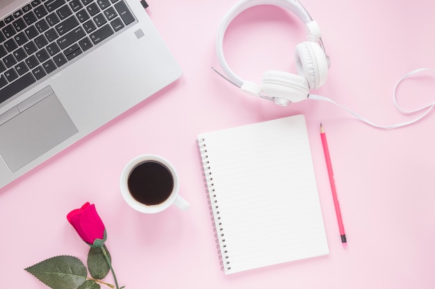 Rosa; xícara de café; fone de ouvido; computador portátil; bloco de notas em espiral e lápis em fundo rosa