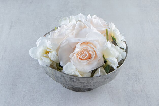 Rosas brancas em uma tigela de ferro, na mesa branca.