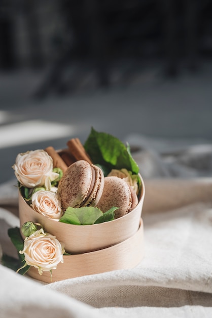 Foto grátis rosas e canela com macaroons no recipiente sobre a toalha de mesa