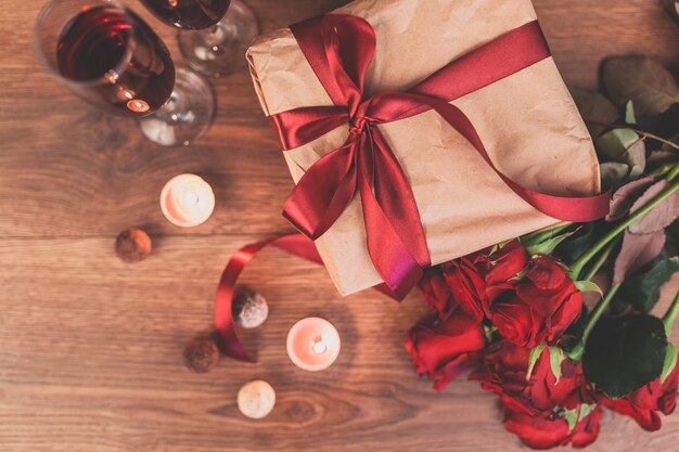 Rosas em uma mesa de madeira com um presente com um laço vermelho