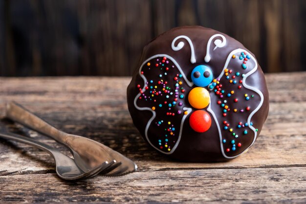 Rosquinha de chocolate com uma borboleta em forma sobre uma tábua rústica de madeira e garfo e faca metálicos prateados