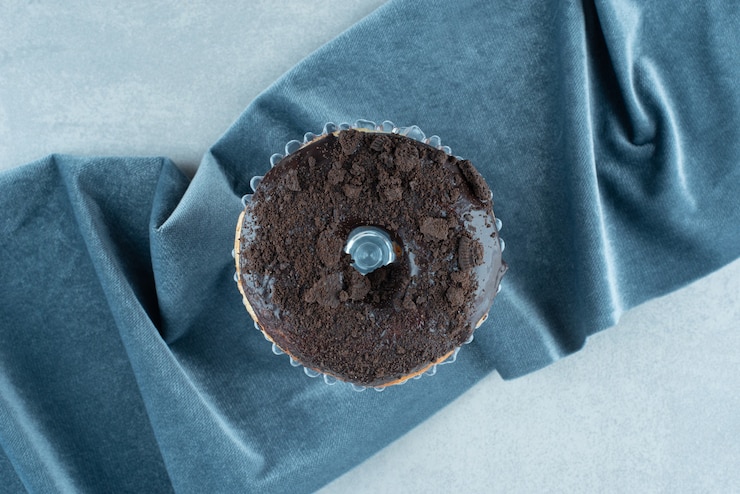 Foto grátis rosquinha única em uma pequena travessa de vidro na toalha de mesa enrugada no mármore.