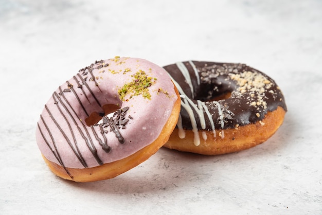 Foto grátis rosquinhas rosa e chocolate com creme e migalhas de noz na superfície branca.