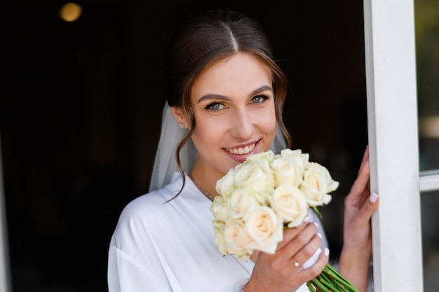 Foto grátis rosto de retrato de jovem noiva sorridente com um buquê com flores brancas linda garota com maquiagem nupcial e penteado olhando para a câmera manhã nupcial preparando a festa do dia do casamento