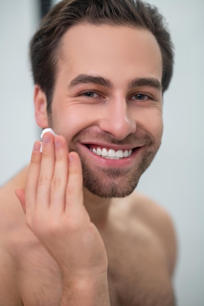 Rotina matinal. homem sorridente limpando o rosto no espelho