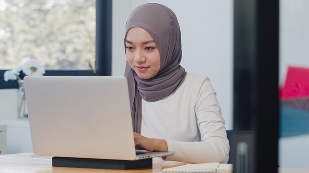 Roupa casual de linda senhora muçulmana asiática trabalhando usando o laptop no escritório normal novo e moderno.