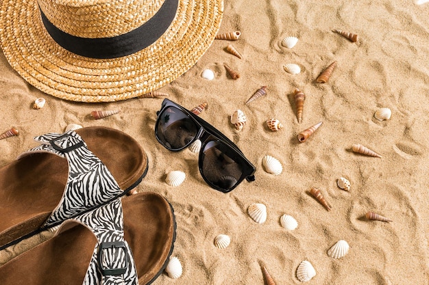 Foto grátis roupas de praia de verão, chinelos, chapéu, óculos escuros e conchas na praia de areia.