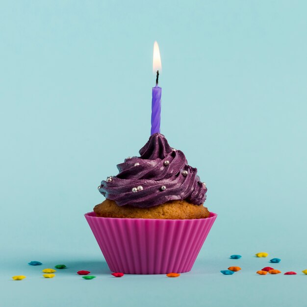 Roxas velas acesas em muffins decorativos com granulado colorido estrela contra o pano de fundo azul